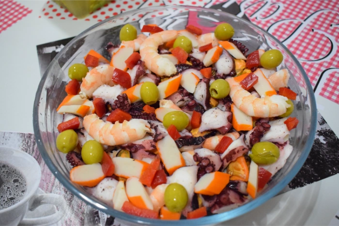 Salpicón de marisco recién mezclado en un bol de cristal, con langostinos, pulpo, pimiento y aceitunas antes del reposo