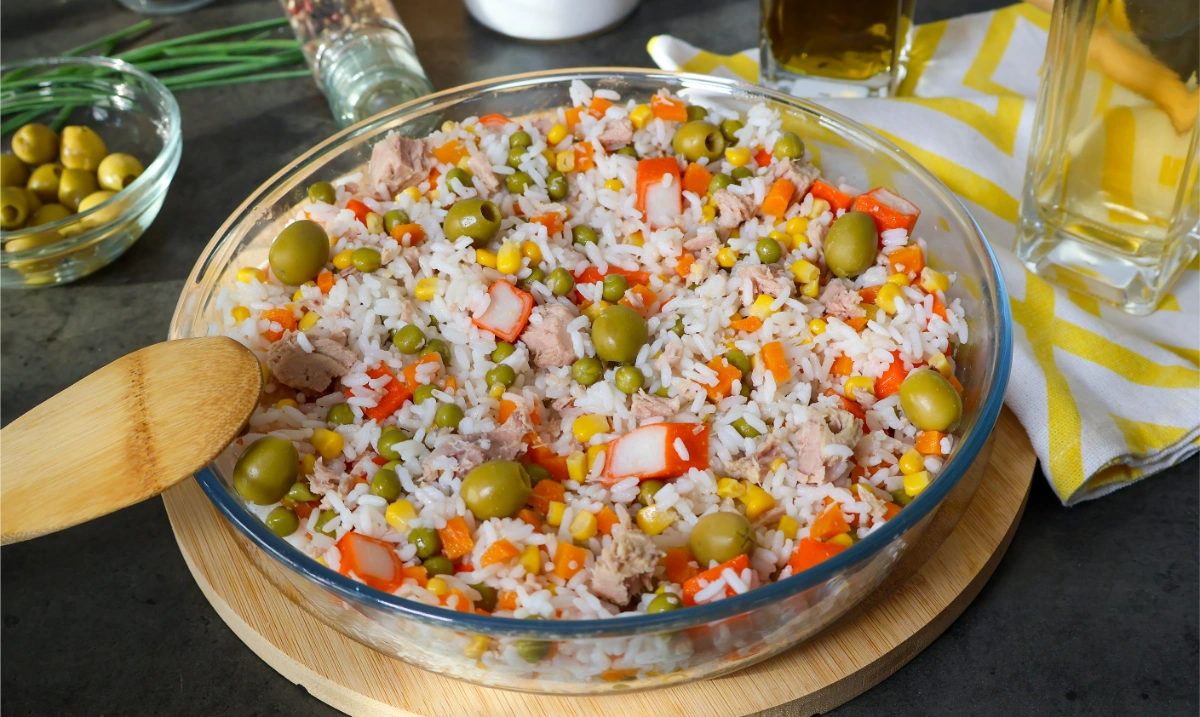 Ensalada de arroz con atún, guisantes, maíz, zanahoria, surimi y aceitunas en una fuente