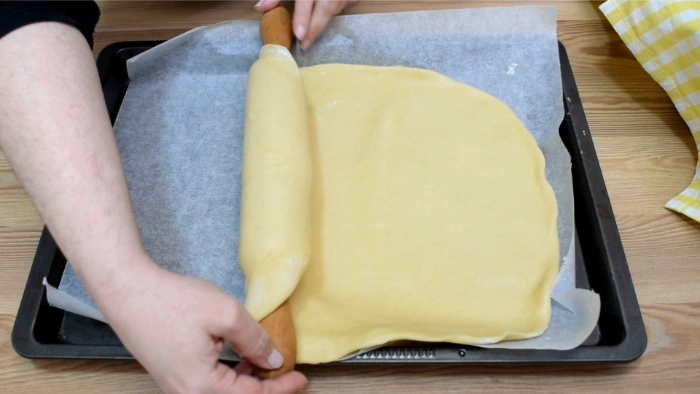 Extendiendo la masa base del hornazo de Salamanca con rodillo sobre bandeja de horno forrada con papel vegetal