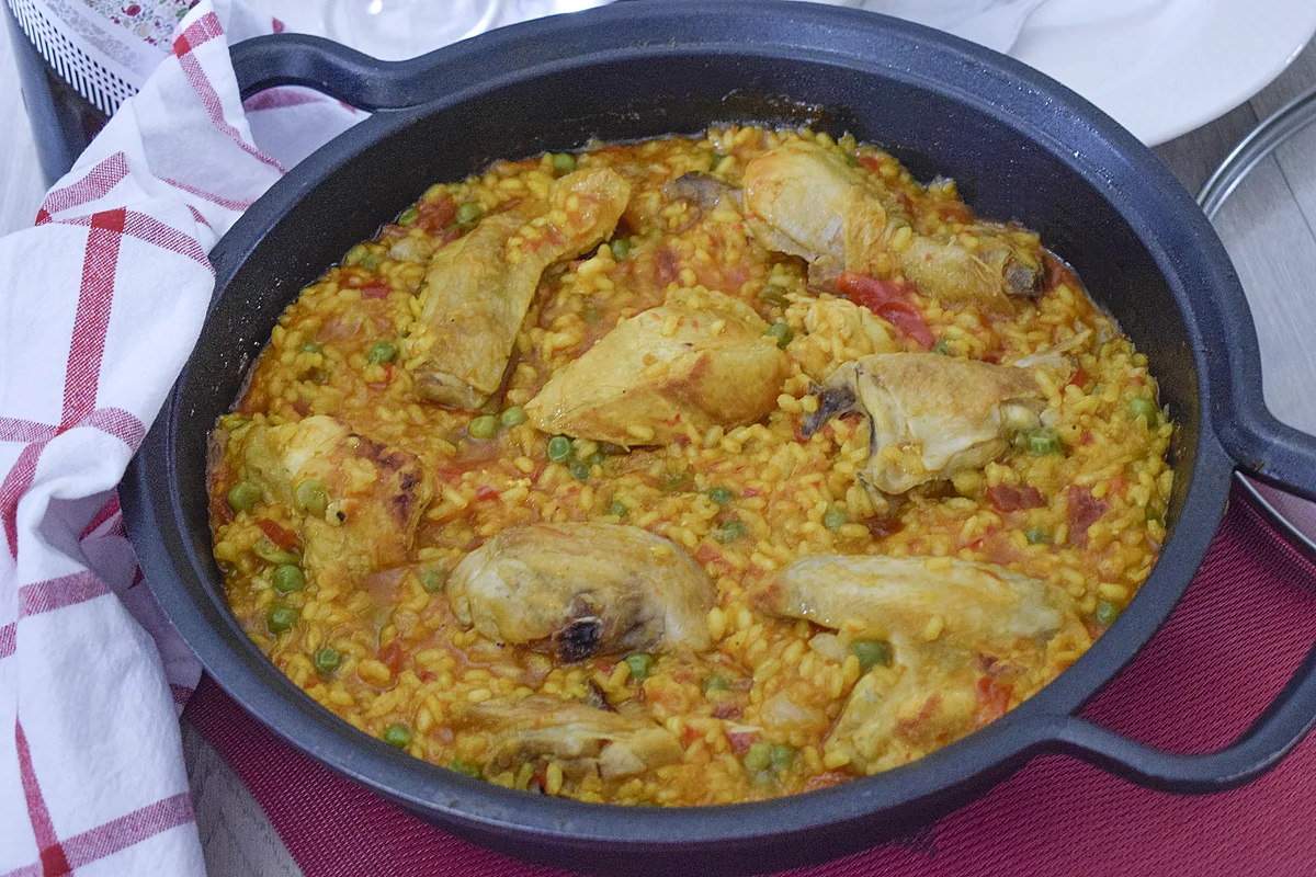 Arroz con pollo y verduras servido en una cazuela negra, con pollo dorado y arroz meloso con guisantes y pimientos. Receta casera fácil y saludable.