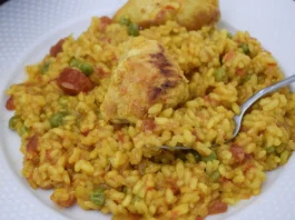 Primer plano del arroz con pollo y verduras en una cuchara, mostrando su textura melosa .