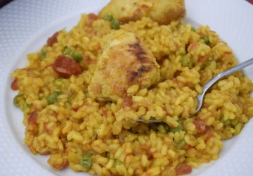 Primer plano del arroz con pollo y verduras en una cuchara, mostrando su textura melosa .