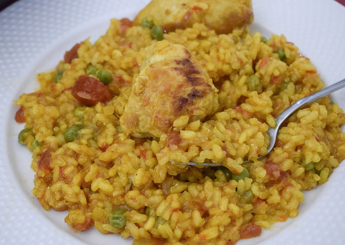 Primer plano del arroz con pollo y verduras en una cuchara, mostrando su textura melosa .