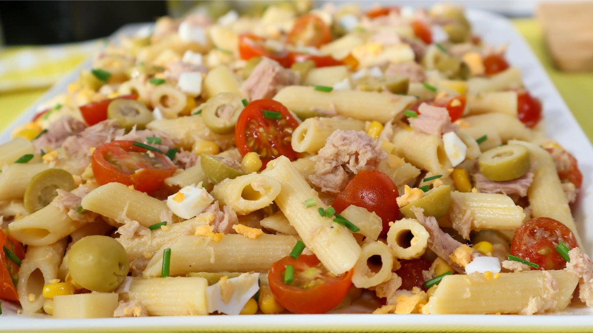 Primer plano de ensalada de pasta con atún, cherrys, aceitunas, maíz y huevo picado