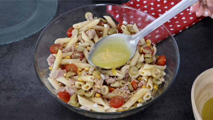Cuchara vertiendo vinagreta sobre la ensalada de pasta con atún, cherrys y aceitunas