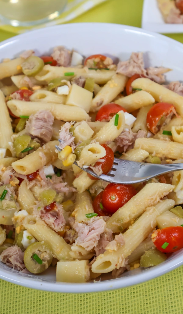 Tenedor con un bocado de ensalada de pasta con atún, cherry y aceitunas sobre el bol