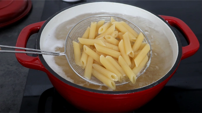 Macarrones cocidos al dente recogidos con una espumadera sobre la olla