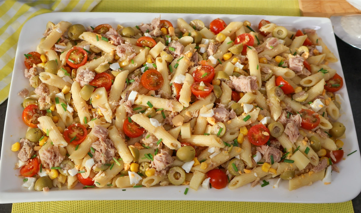 Ensalada de pasta fría con atún, maíz, tomate y aceitunas vista cenital en fuente rectangular