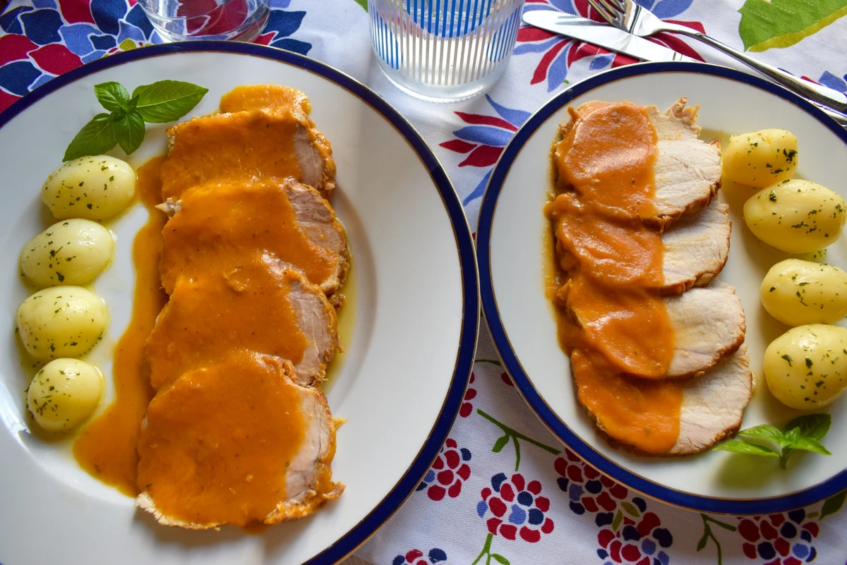 Platos de lomo de cerdo en salsa con patatas cocidas, presentados sobre mantel de flores
