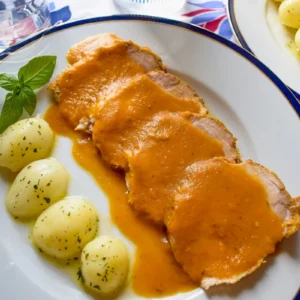 Lomo de cerdo en salsa con patatas cocidas servido en plato blanco