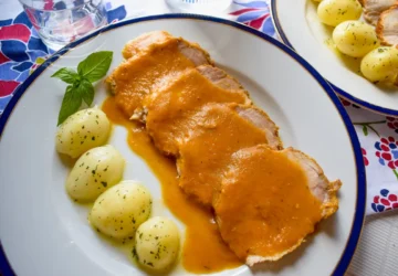 Lomo de cerdo en salsa con patatas cocidas servido en plato blanco