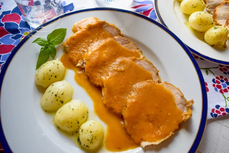 Lomo de cerdo en salsa con patatas cocidas servido en plato blanco