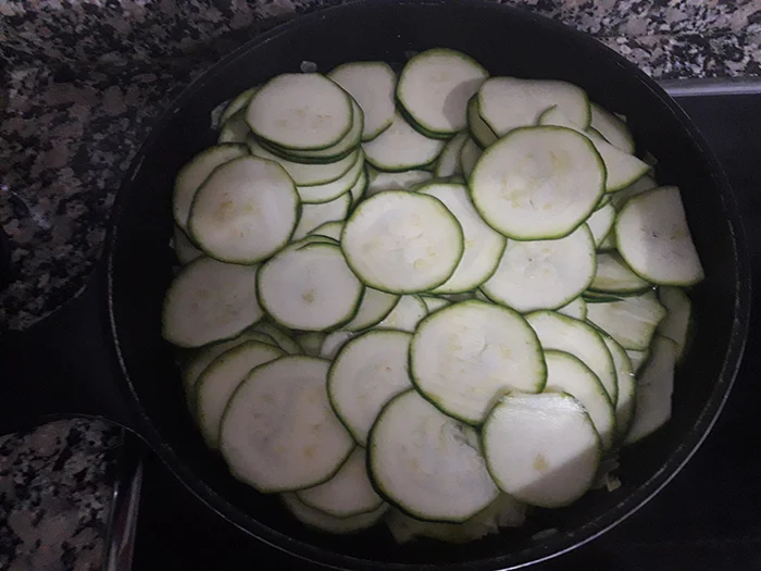 Rodajas de calabacín cocinándose en sartén sobre cama de cebolleta