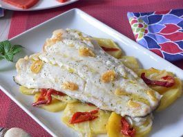 Bacalao al horno con patatas, piquillos y sofrito de ajos en plato blanco