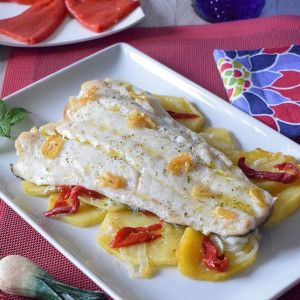 Bacalao al horno con patatas, piquillos y sofrito de ajos en plato blanco