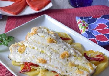 Bacalao al horno con patatas, piquillos y sofrito de ajos en plato blanco