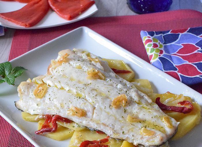 Bacalao al horno con patatas, piquillos y sofrito de ajos en plato blanco