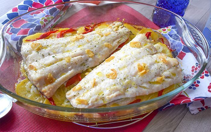 Fuente de cristal con bacalao al horno, patatas y piquillos recién salidos del horno
