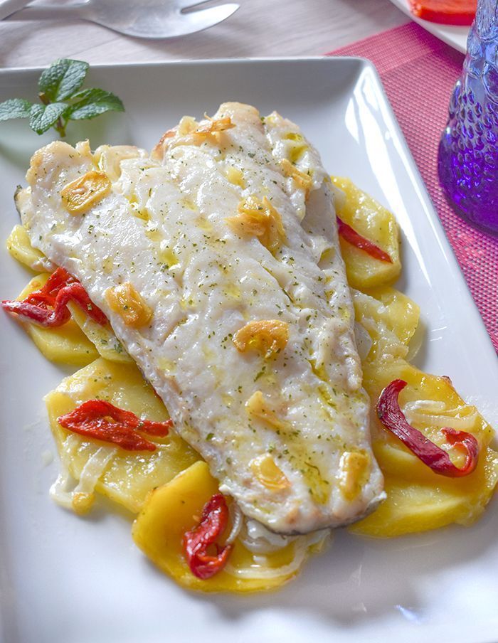 Bacalao al horno con patatas y piquillos servido en plato blanco con ajos dorados