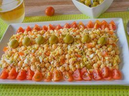 Ensalada de garbanzos con atún, huevo y aceitunas en fuente blanca, bordeada de tomate cherry