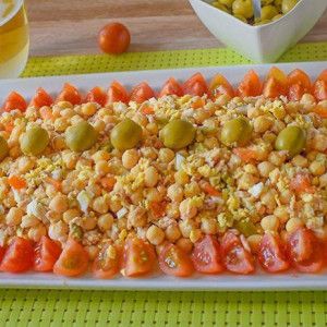 Ensalada de garbanzos con atún, huevo y aceitunas en fuente blanca, bordeada de tomate cherry