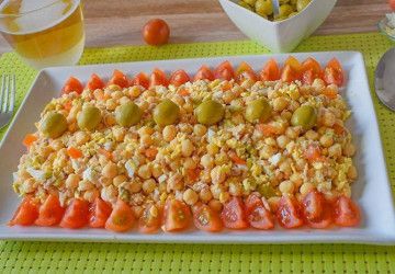 Ensalada de garbanzos con atún, huevo y aceitunas en fuente blanca, bordeada de tomate cherry