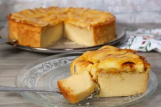 Porción de tarta de manzana con cuchara mostrando su textura cremosa. Al fondo, el resto de la tarta.