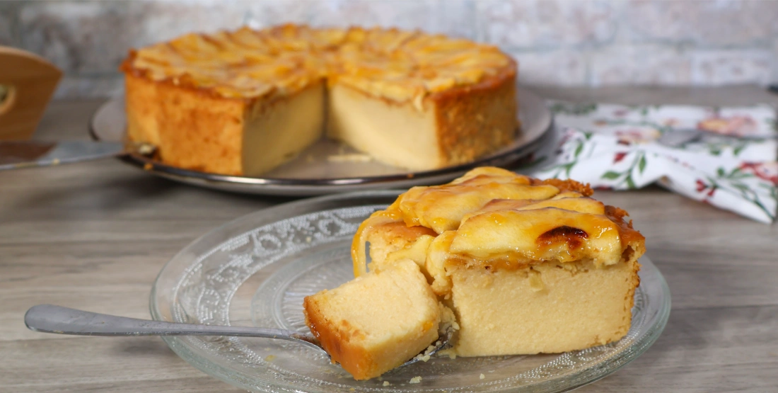 Porción de tarta de manzana con cuchara mostrando su textura cremosa. Al fondo, el resto de la tarta.