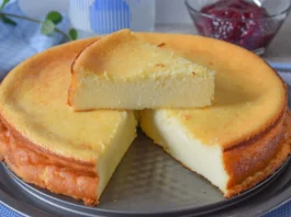 Tarta de queso al horno con una porción levantada mostrando el interior cremoso y cuenco de mermelada de frambuesa al fondo