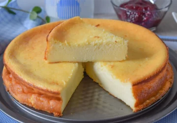 Tarta de queso al horno con una porción levantada mostrando el interior cremoso y cuenco de mermelada de frambuesa al fondo