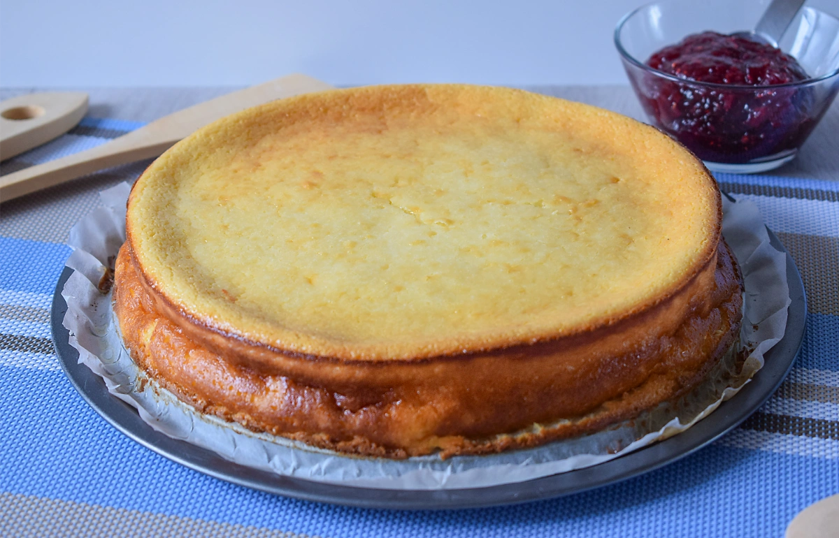 Tarta de queso al horno recién desmoldada con superficie dorada y mermelada de frambuesa al fondo