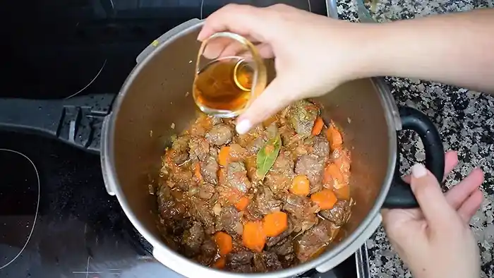 Añadiendo vino al estofado de ternera con zanahoria y laurel