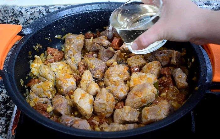 Añadiendo vino blanco al sofrito de carne y chorizo