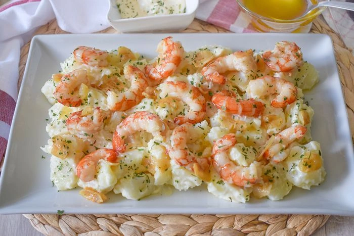 Patatas arrieras cocidas con gambas al ajillo y alioli casero servidas en fuente rectangular blanca, con cuencos de alioli y aceite de oliva al fondo