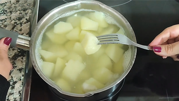 Patatas troceadas en gajos cociéndose en una cazuela con agua, comprobando el punto de cocción con un tenedor