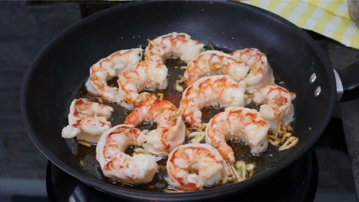 Gambones pelados salteados con ajo en una sartén antiadherente, con el aceite con pimentón del sofrito