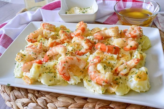 Patatas arrieras con gambas y alioli casero servidas en fuente rectangular blanca, con un cuenco de alioli y otro de aceite de oliva al fondo