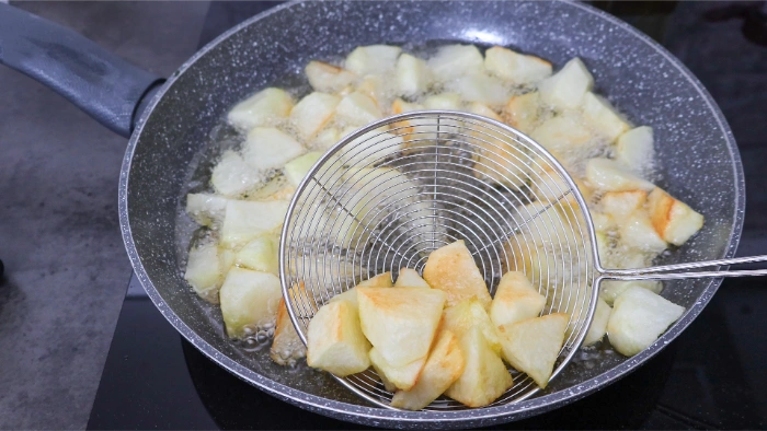 Patatas en gajos friéndose en abundante aceite en una sartén, retirándose con una araña de cocina