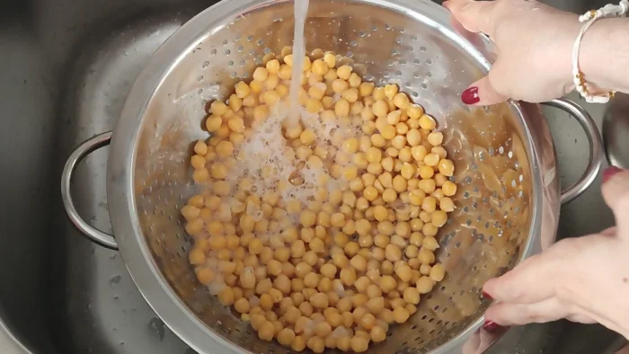 Enjuagando garbanzos cocidos de bote en escurridor bajo el grifo