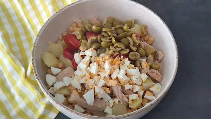 Bol con ingredientes de ensalada de garbanzos antes de mezclar: patatas, atún, huevo, aceitunas y cherry