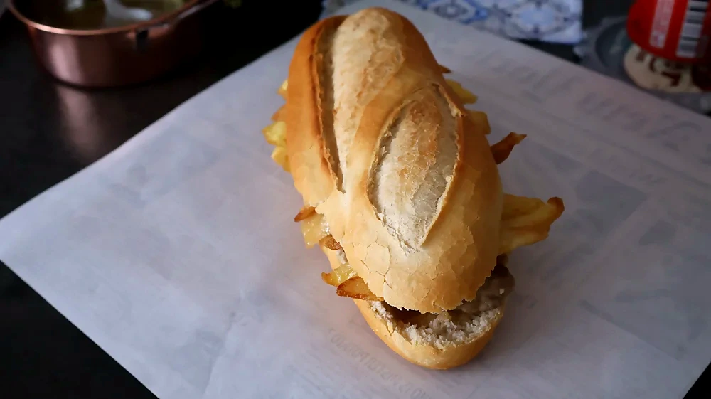 Bocadillo de solomillo al whisky con patatas fritas caseras, servido entero sobre papel de cocina.