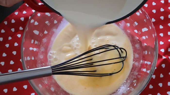 Vertiendo leche caliente sobre mezcla de huevos para hacer crema pastelera sin grumos