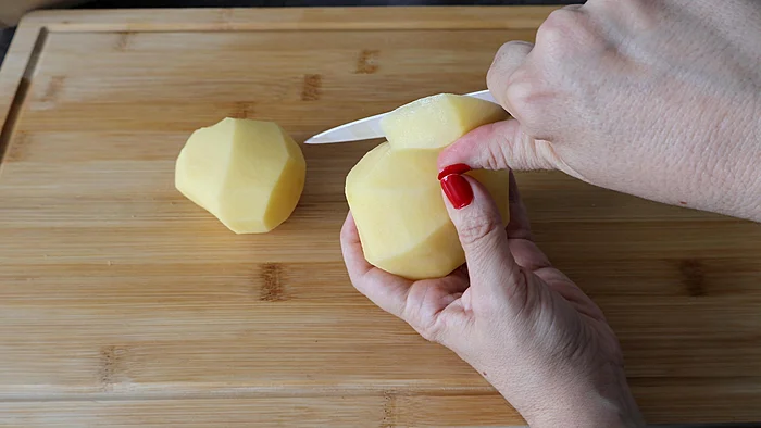 Mano pelando patatas con cuchillo sobre tabla de madera