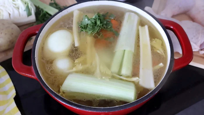 Olla con agua, pollo, y verduras hirviendo para hacer caldo de pollo casero