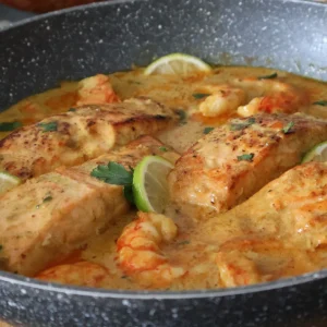 Salmón al curry con gambas servido en sartén con salsa cremosa y lima