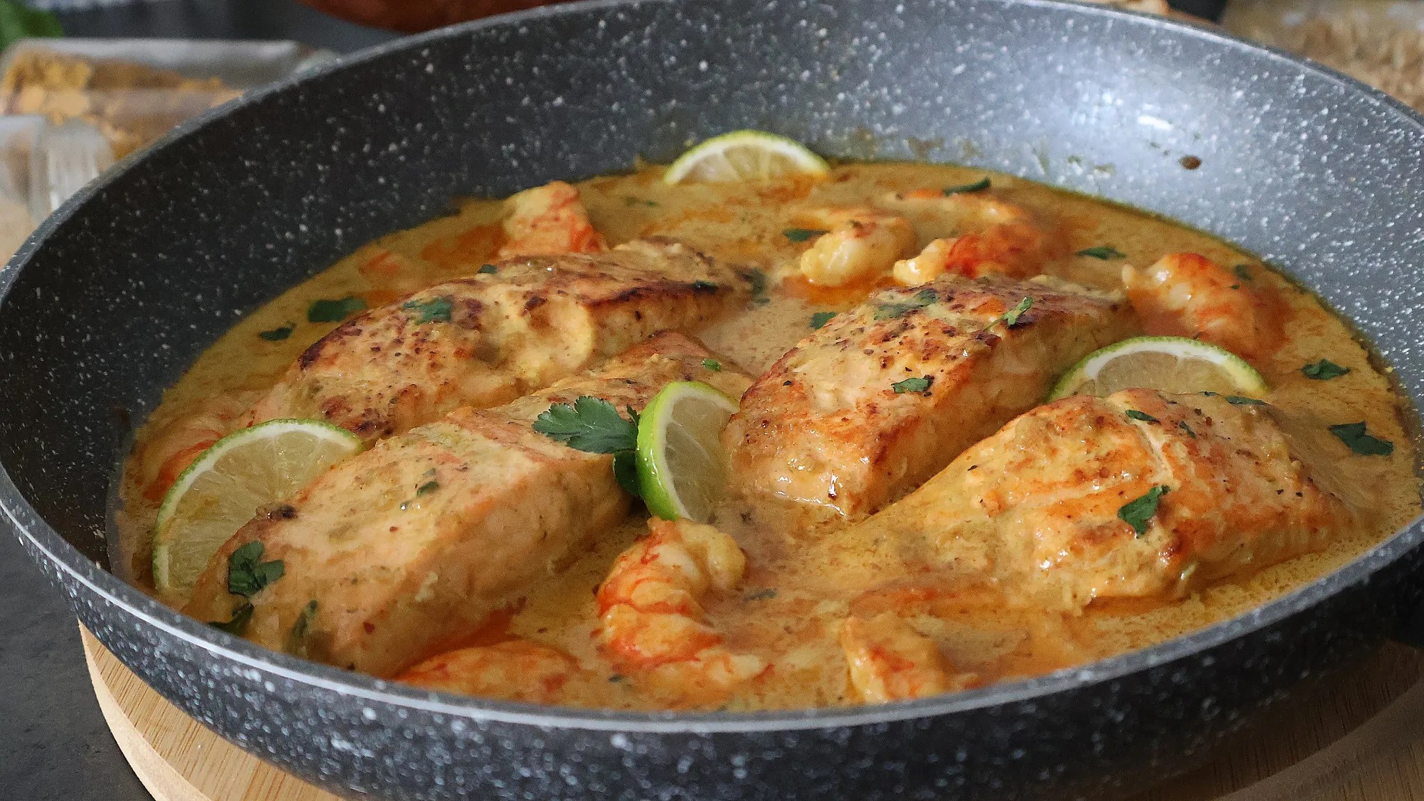 Salmón al curry con gambas servido en sartén con salsa cremosa y lima
