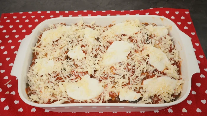 Fuente con berenjenas a la parmesana lista para gratinar, cubierta de queso rallado y mozzarella.