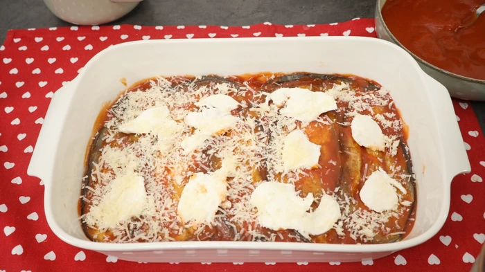 Capa de berenjenas fritas con salsa de tomate y queso, lista para seguir montando la receta.