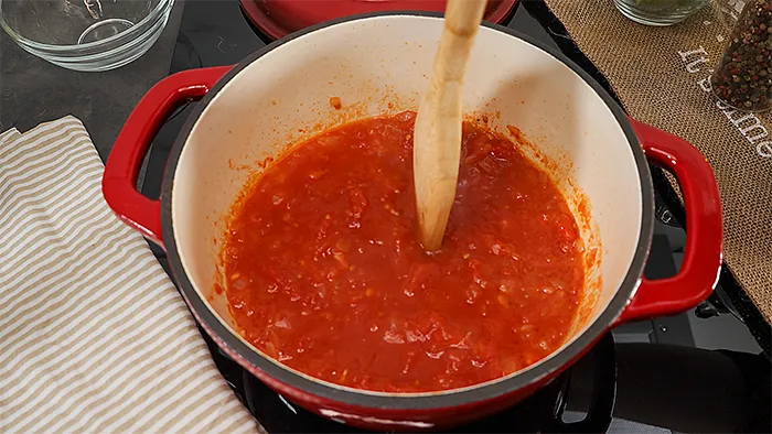 Salsa de tomate cocinándose con trozos visibles y cuchara de madera