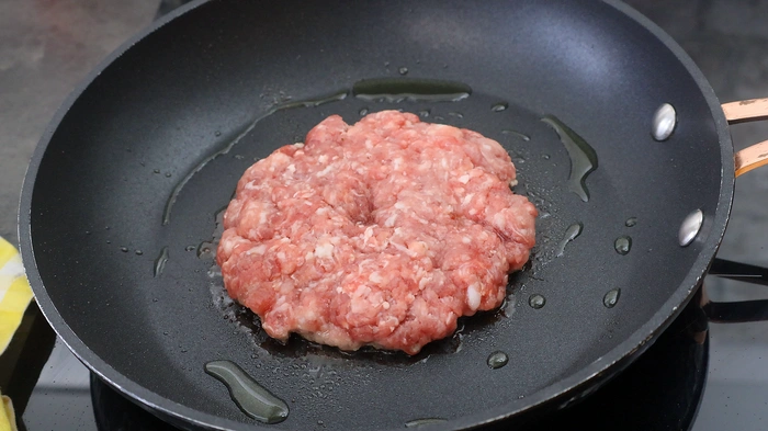 Hamburguesa cruda en la sartén con aceite de oliva